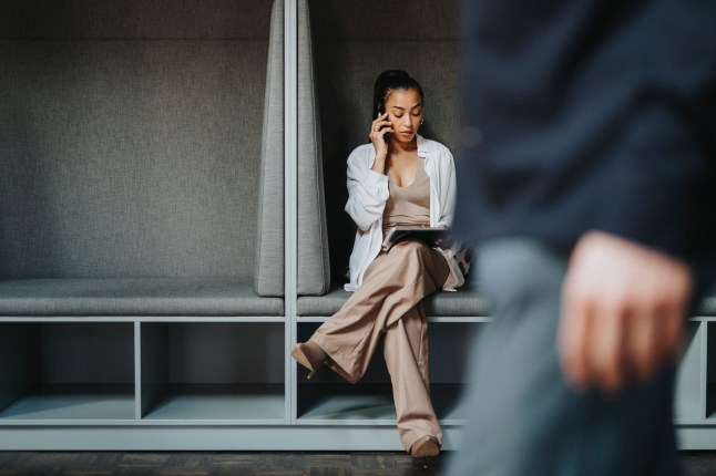Female entrepreneur talking on smart phone while sitting with legs crossed in booth at office