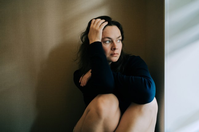 Woman sitting on floor with hands in hair feeling anxious, stressed, and overwhelmed