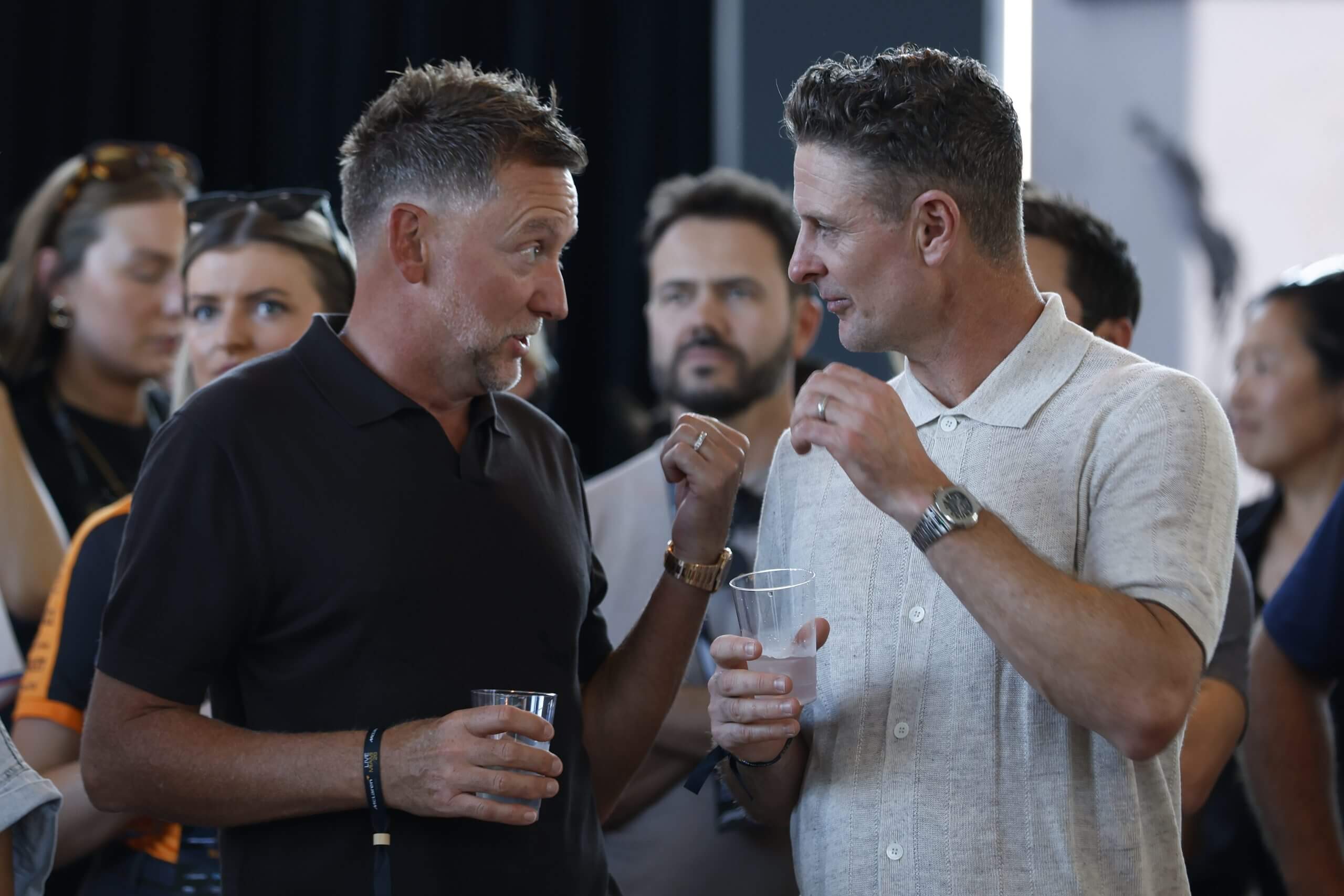 Ian Poulter and Justin Rose hold drinks and talk with other people in the background.