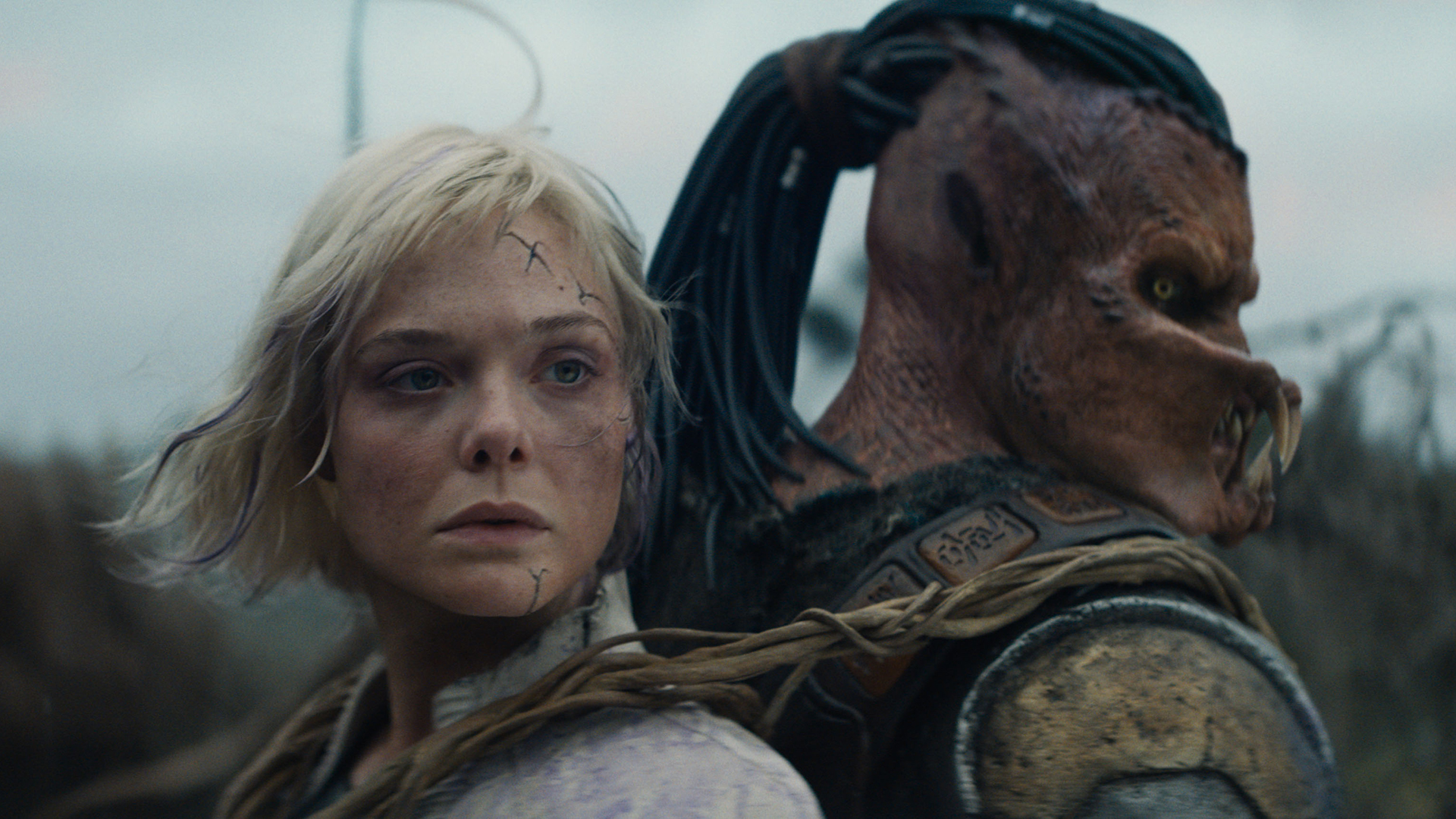 Thia (Elle Fanning) and Dek (Dimitrius Schuster-Koloamatangi) standing back to back in Predator: Badlands