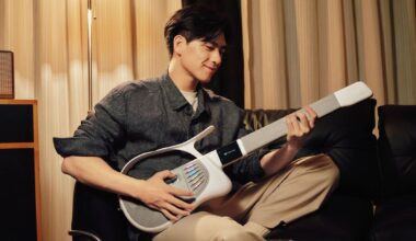 A man sits on a sofa, playing the TemPolor Melo-D guitar