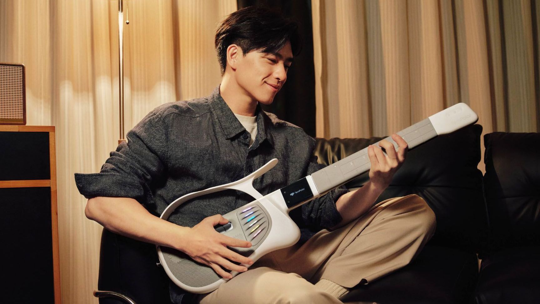 A man sits on a sofa, playing the TemPolor Melo-D guitar