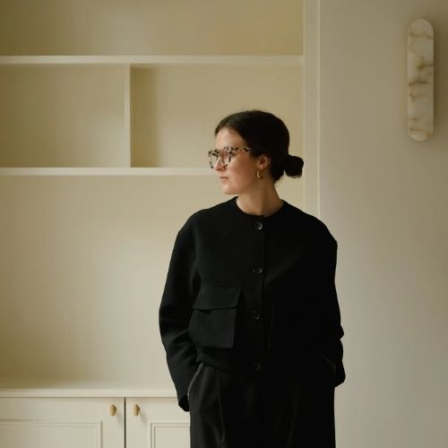 A woman wearing all black standing in a butter yellow room.