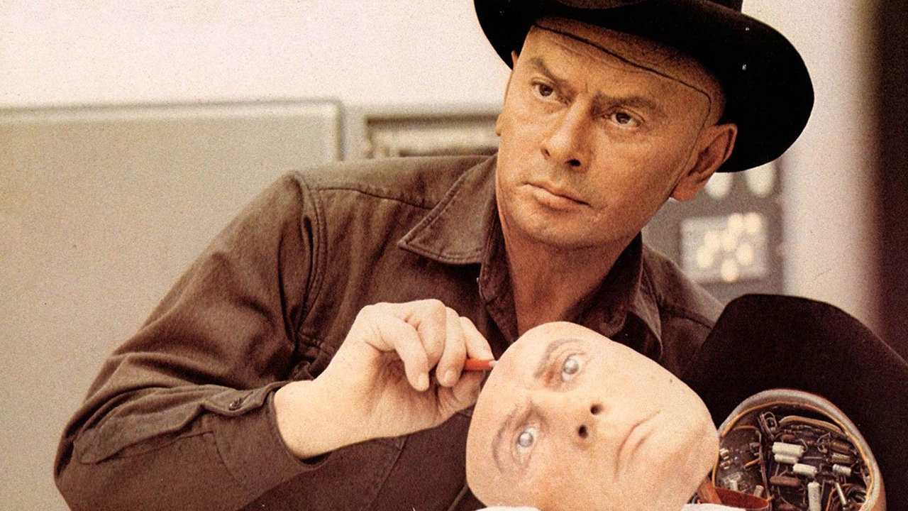 Still from the movie "Westworld" (1973). A human robot wearing a black cowboy hat is opening up the face of another human robot, exposing the wires inside.