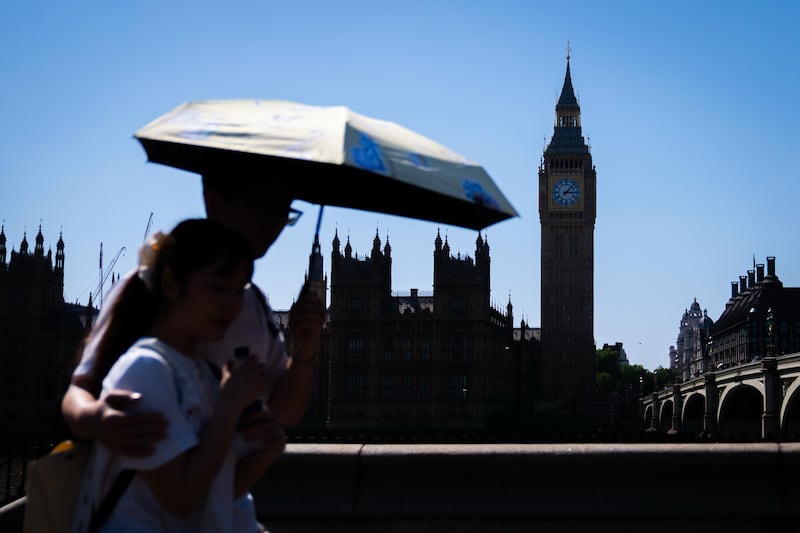 Tourists shelter from the hot weather beneath an umbrella on Westminster Bridge, central London. Photograph: James Manning/PA 
