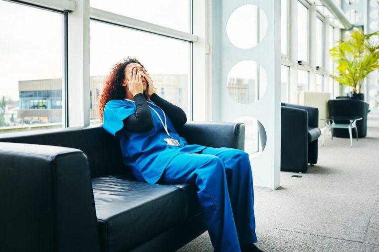 Stressed young female medical professional sitting on a sofa and taking break from work in hospital
