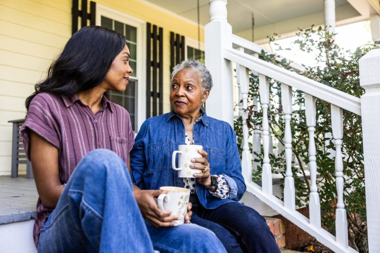 Senior woman and adult daughter having coffee on front porch of rural farm home