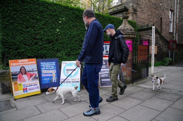 Men and their dogs look at signs outside the polling station at St James Church hall in Inverleith, Edinburgh, as voters start to cast their votes in the 2026 Holyrood elections. Picture date: Thursday May 7, 2026. PA Photo. Photo credit should read: Jane Barlow/PA Wire