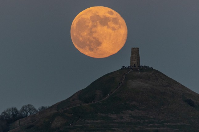 GLASTONBURY, UNITED KINGDOM - JANUARY 03: A full Wolf Moon supermoon rises behind Glastonbury Tor as people gather to watch the first full moon of the year on January 3, 2026 in Glastonbury, England. Tonight's full moon is the first supermoon of 2026, so called because it is when the moon is closest to the Earth and is also known as the Wolf Moon, because wolves don't hibernate in winter, and so the howling of wolves in the first month of the year would have historically been more noticeable. (Photo by Matt Cardy/Getty Images)