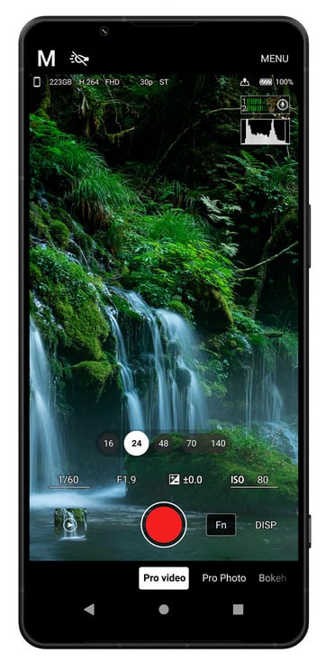 A smartphone screen displays a camera app in manual mode, focused on a lush green waterfall scene. Various camera settings like ISO, shutter speed, and exposure are shown, with a large red recording button at the center.