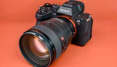 A Sony Alpha 7R mirrorless camera with a large zoom lens attached, placed on an orange surface with visible control dials and logos.