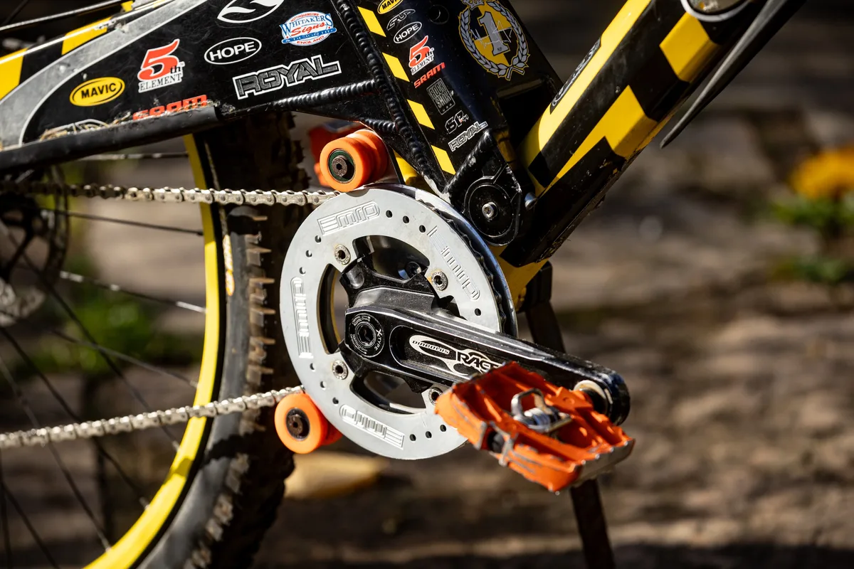 Close-up of Steve Peat’s Orange 224 Bumblebee downhill bike showing the Race Face crank, MRP chainguide, orange pedals and yellow-rimmed rear wheel.