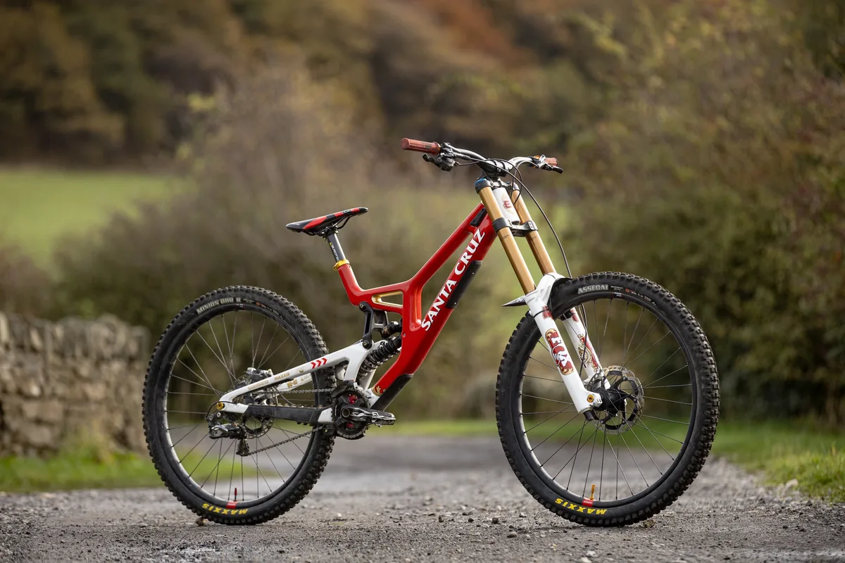 Steve Peat’s red and white Santa Cruz V10 downhill bike photographed on a gravel track, with Fox 40 forks and 29in wheels.