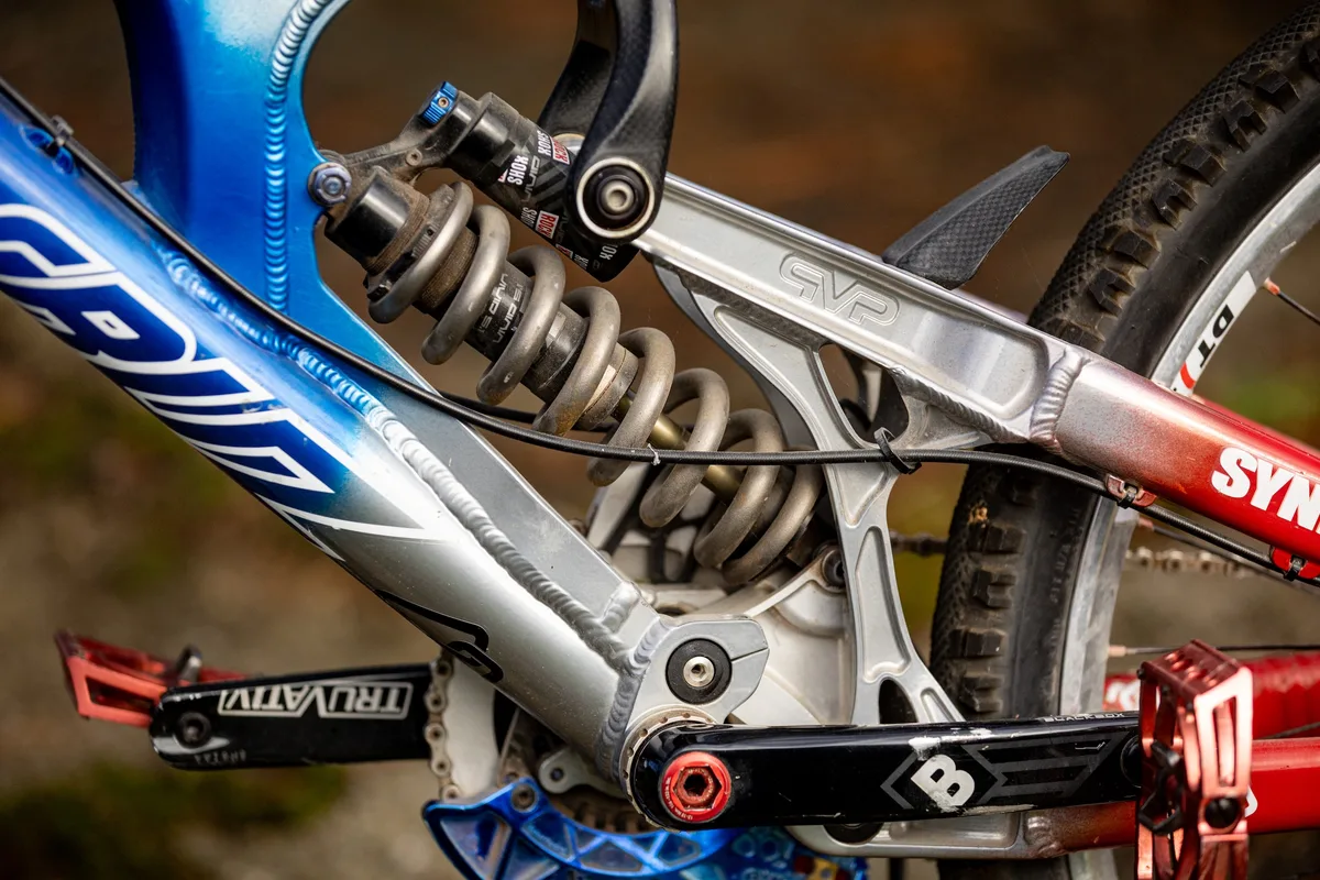 Close-up of Steve Peat’s blue and red Santa Cruz V10 downhill bike showing the coil shock, VPP linkage and aluminium frame detail.