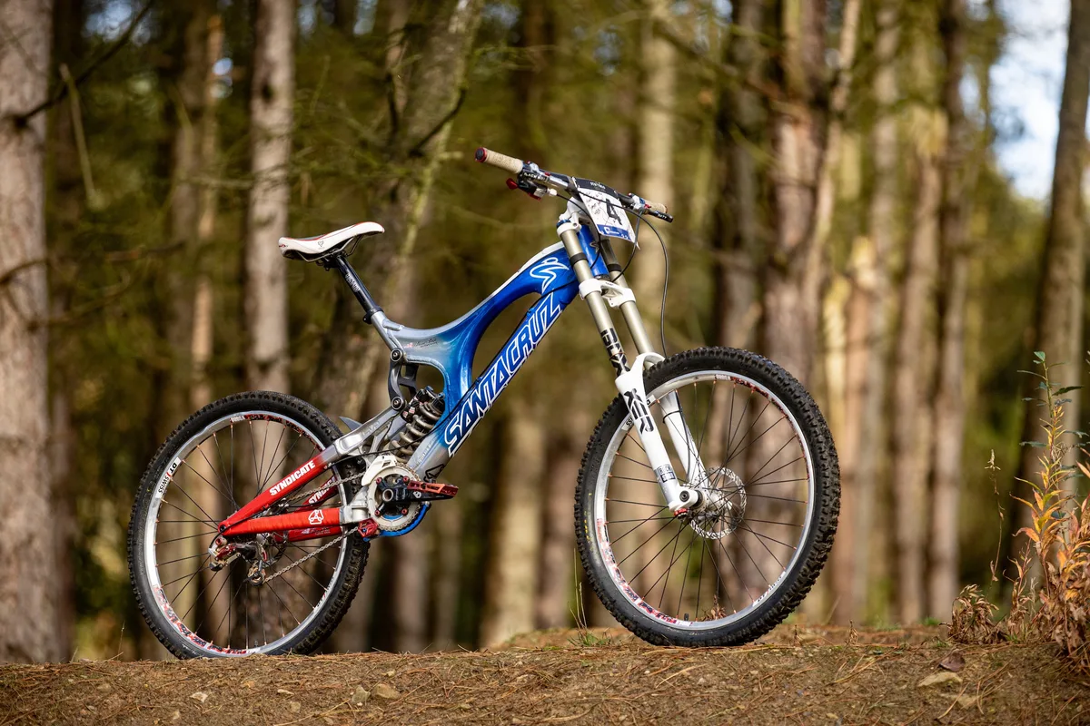 Steve Peat’s blue and red Santa Cruz V10 downhill bike photographed in woodland, with RockShox BoXXer forks and 26in wheels.