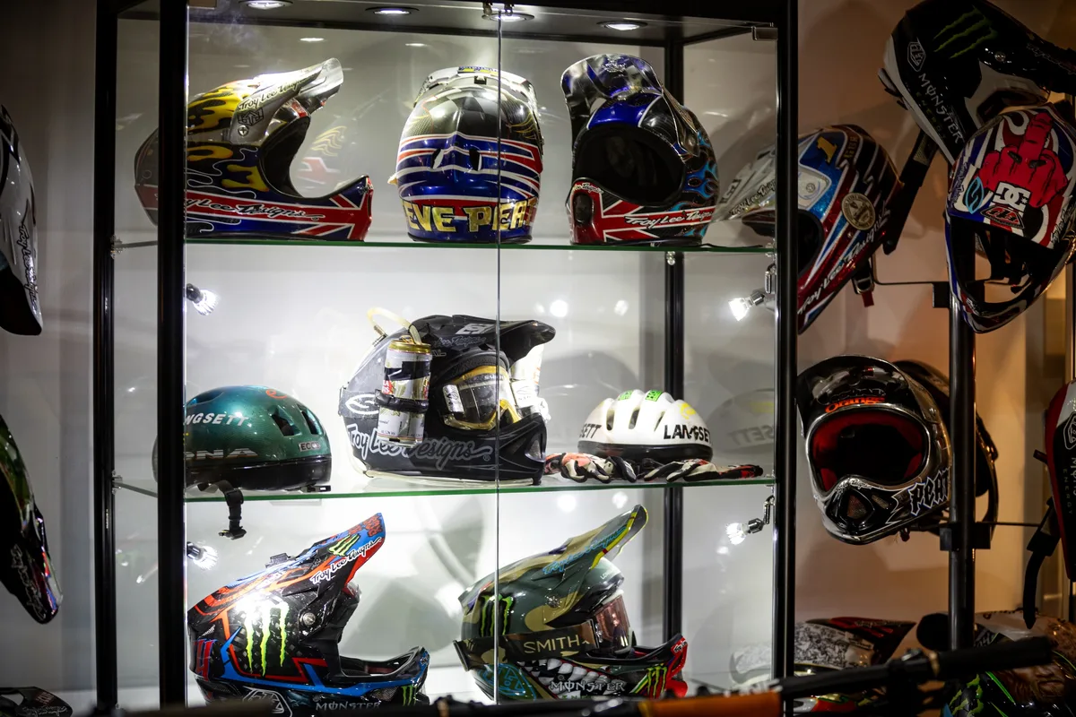Steve Peat’s mountain bike helmet collection displayed in a glass cabinet, including Troy Lee Designs, Monster Energy and race-livery helmets.