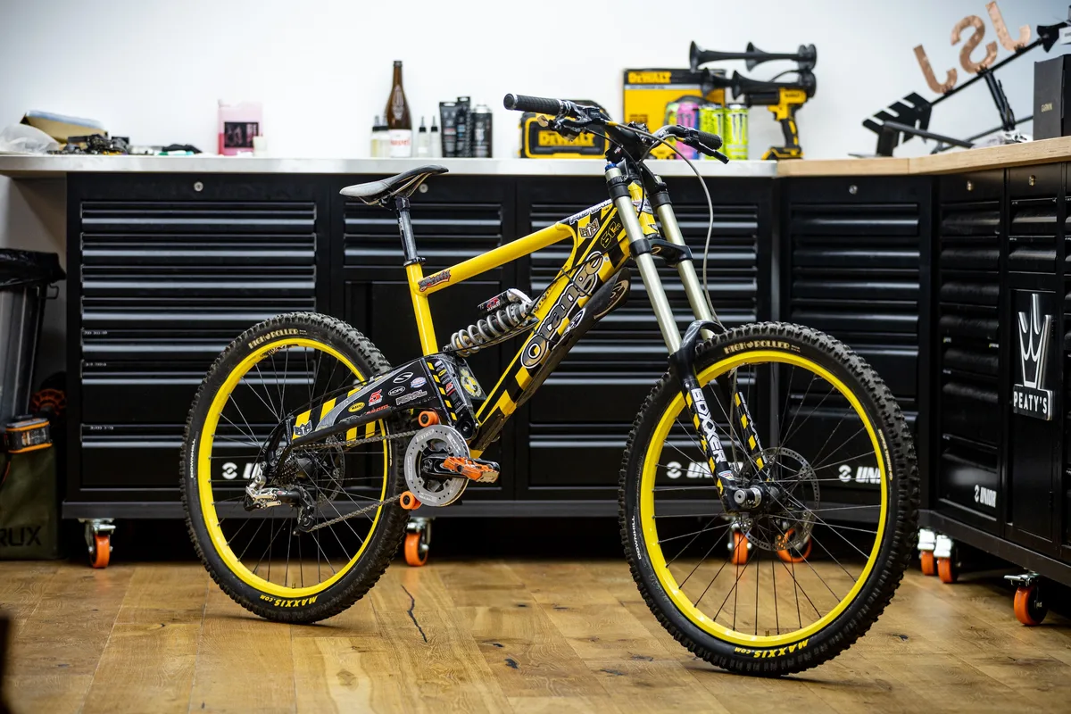 Steve Peat’s yellow and black Orange 224 downhill bike displayed in his workshop, with matching yellow rims and RockShox BoXXer forks.