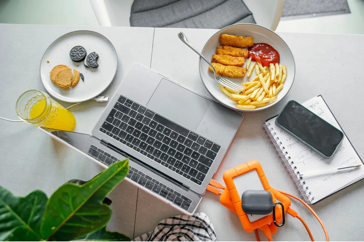 A meal of fish fingers, chips, ketchup, biscuits and orange juice, eaten at a desk