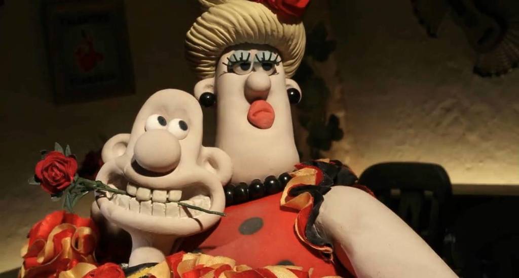 a still from a wallace and gromit film, showing wallace dancing with someone while clutching a rose between his teeth