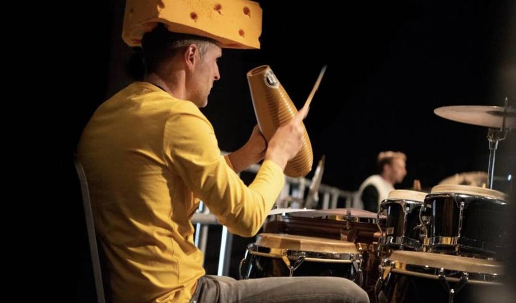a percussionist playing in an orchestra, while dressed as a block of cheese