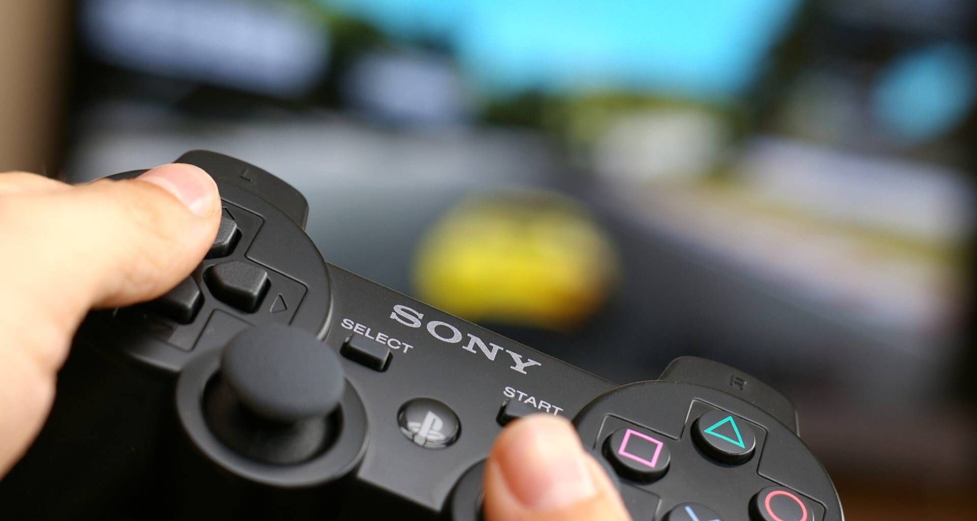 Man's hand holding Sony Dualshock wireless controller while playing Gran Turismo 5 on PlayStation 3.