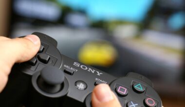 Man's hand holding Sony Dualshock wireless controller while playing Gran Turismo 5 on PlayStation 3.