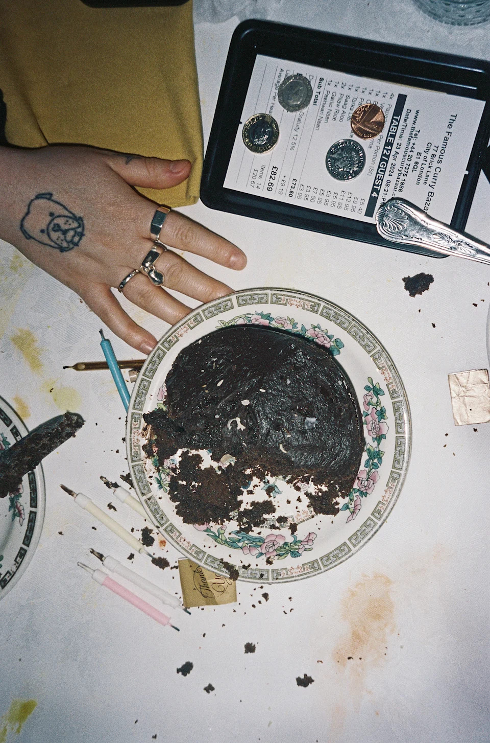 Colour photograph of a half-eaten chocolate cake on a table. Alongside it, there is a menu, some candles and a hand on the table as well