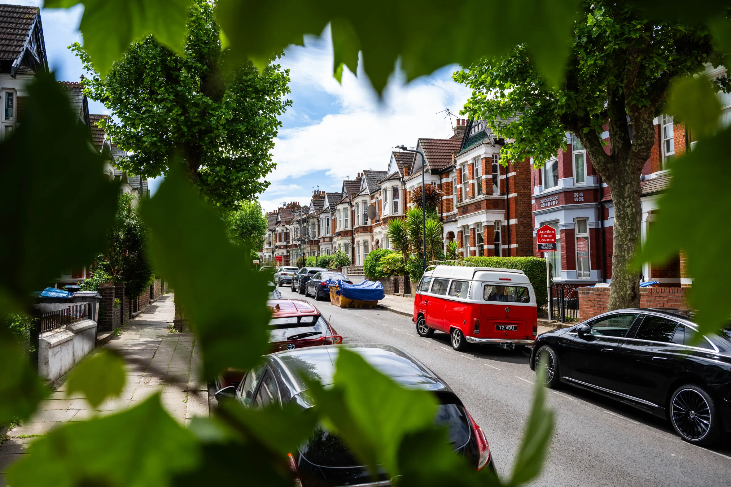 Harlesden Gardens road in London, with affluent residential properties, cars parked along the street, and a red and white vintage van.