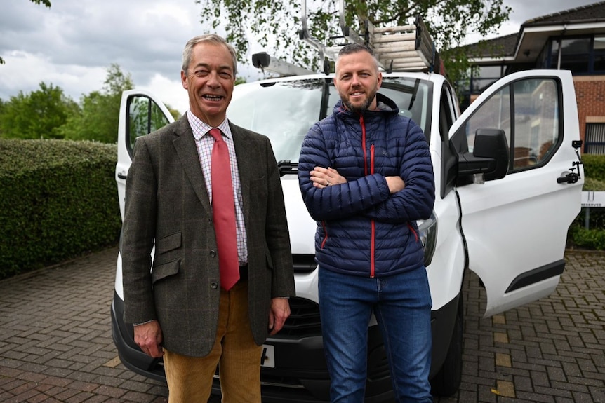 Two men standing near a van and smiling at the camera.