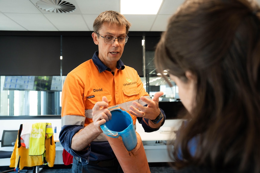 A man in a hi-vis shirt looking at a piece of old pipe