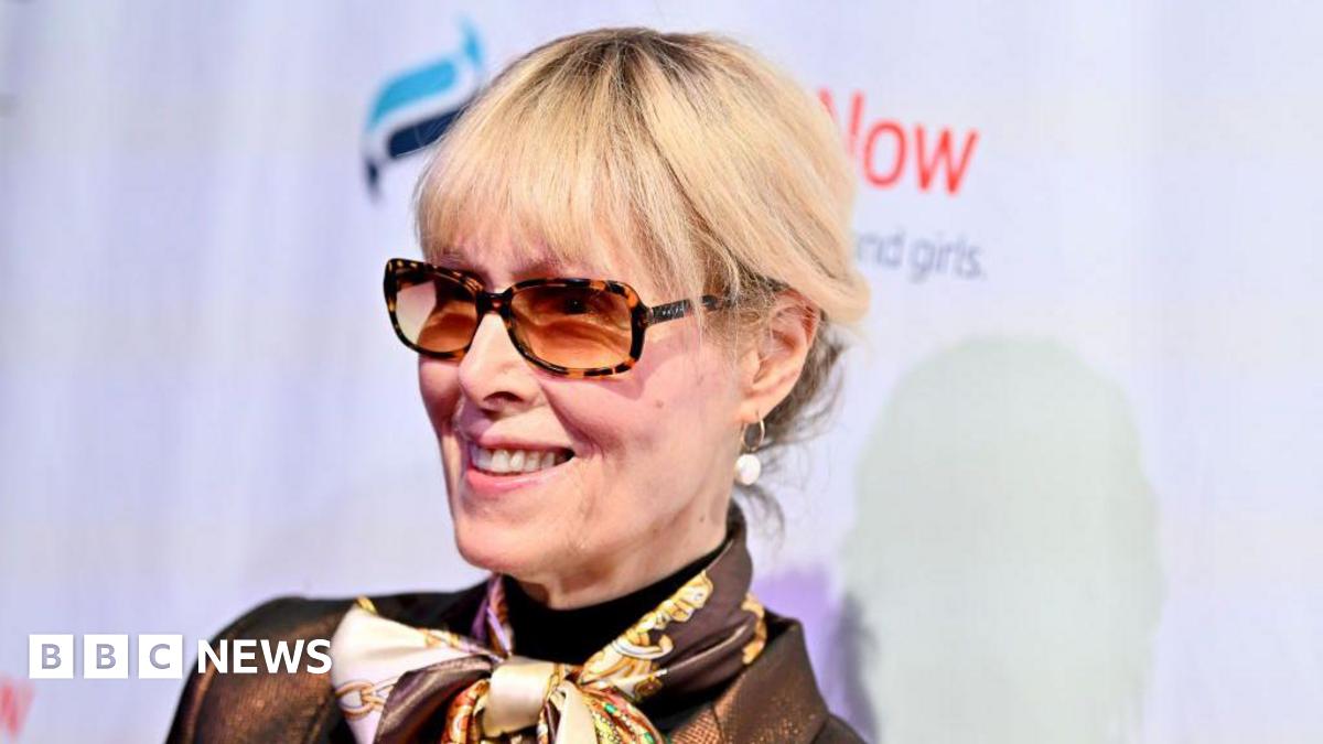 Headshot of E Jean Carroll attending a gala in New York City in 2024. She has blonde hair, and is wearing tortoise-shell patterned sunglasses, gold hoop earrings with pearls, and a neck scarf