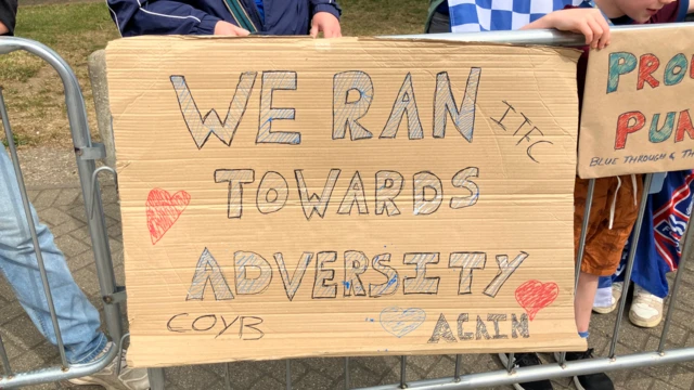 A cardboard sign which says, ITFC, WE RAN TOWARDS ADVERSITY AGAIN