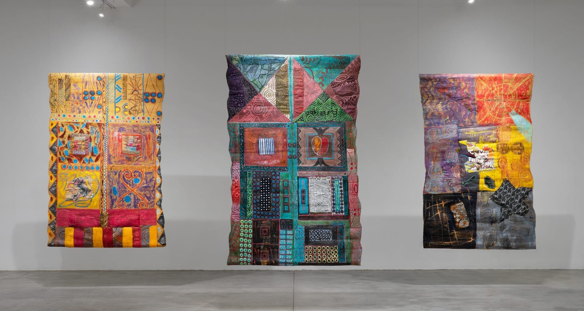 an installation image of three vibrantly painted and stitched abstract compositions by Pacita Abad