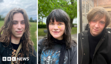 Three young people look directly into the camera lens and pose for a photograph. The photos have been taken separately and have been framed together. Fergus, on the left, has long wavy hair and is sitting in an open green space. Lucian, in the middle, is sat in a park with a leafy tree in the background. They have long hair and a fringe, are wearing two yellow star patches on their cheek and have a nose ring and two lip piercings. Matthew, on the right, is slightly tilting his head while posing indoors with a foosball table and a brick wall in the background. The pictures are separated by two slim white margins.