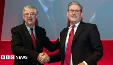 Mark Drakeford shaking hands with Sir Keir Starmer in front of a red background