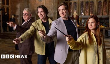Four actors recreating a scene from Harry Potter as they each hold a small sword in front of them as they stand in a line next to each other. There are three men wearing jackets and one woman who is wearing a large yellow shirt.