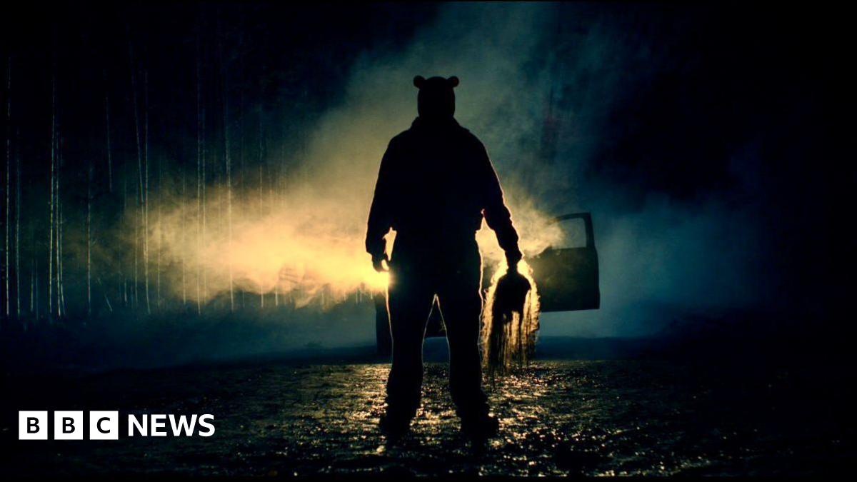 A silhouette of a figure in front of car headlights, at night. He is holding something ominous in his hand.