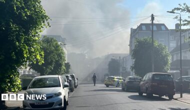 Police tape with smoky skyline beyond residential street with parked cars