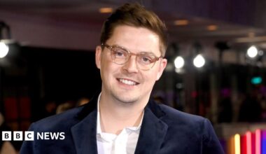 Alex George, who is wearing a blue jacket and glasses