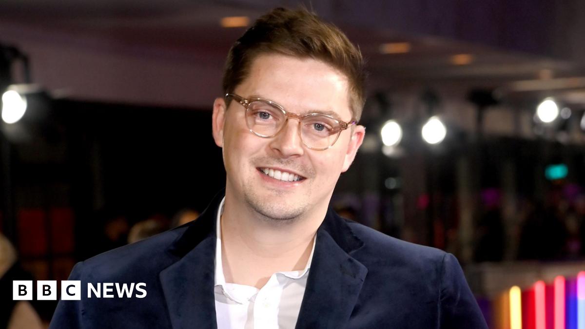 Alex George, who is wearing a blue jacket and glasses