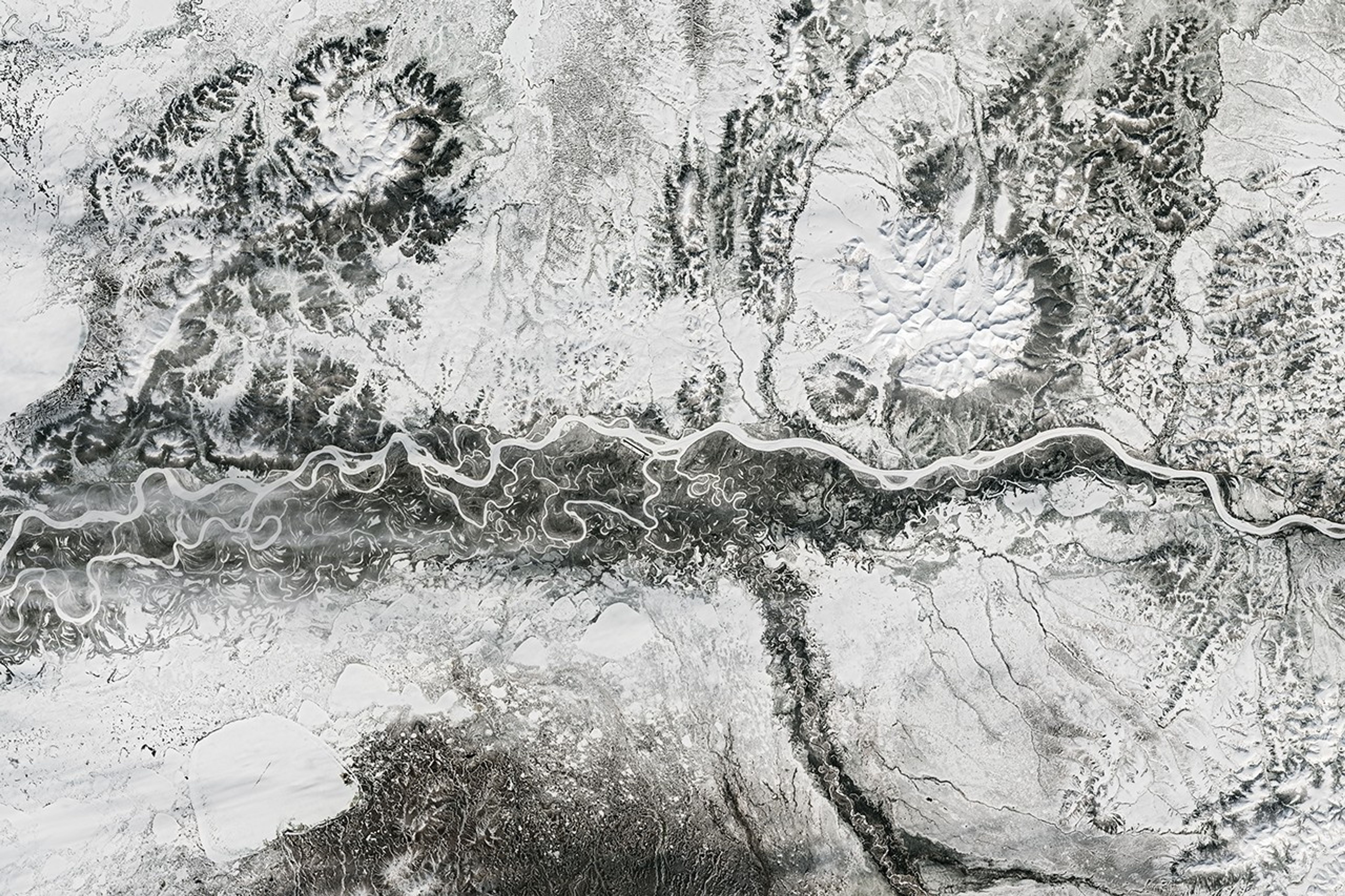 A frozen river winds from east to west past Aniak, Alaska. Nearby meandering channels are also frozen, and much of the surrounding land is snow-covered.