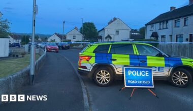 A police cordon in the area. There is a police car, tape and a road closed sign