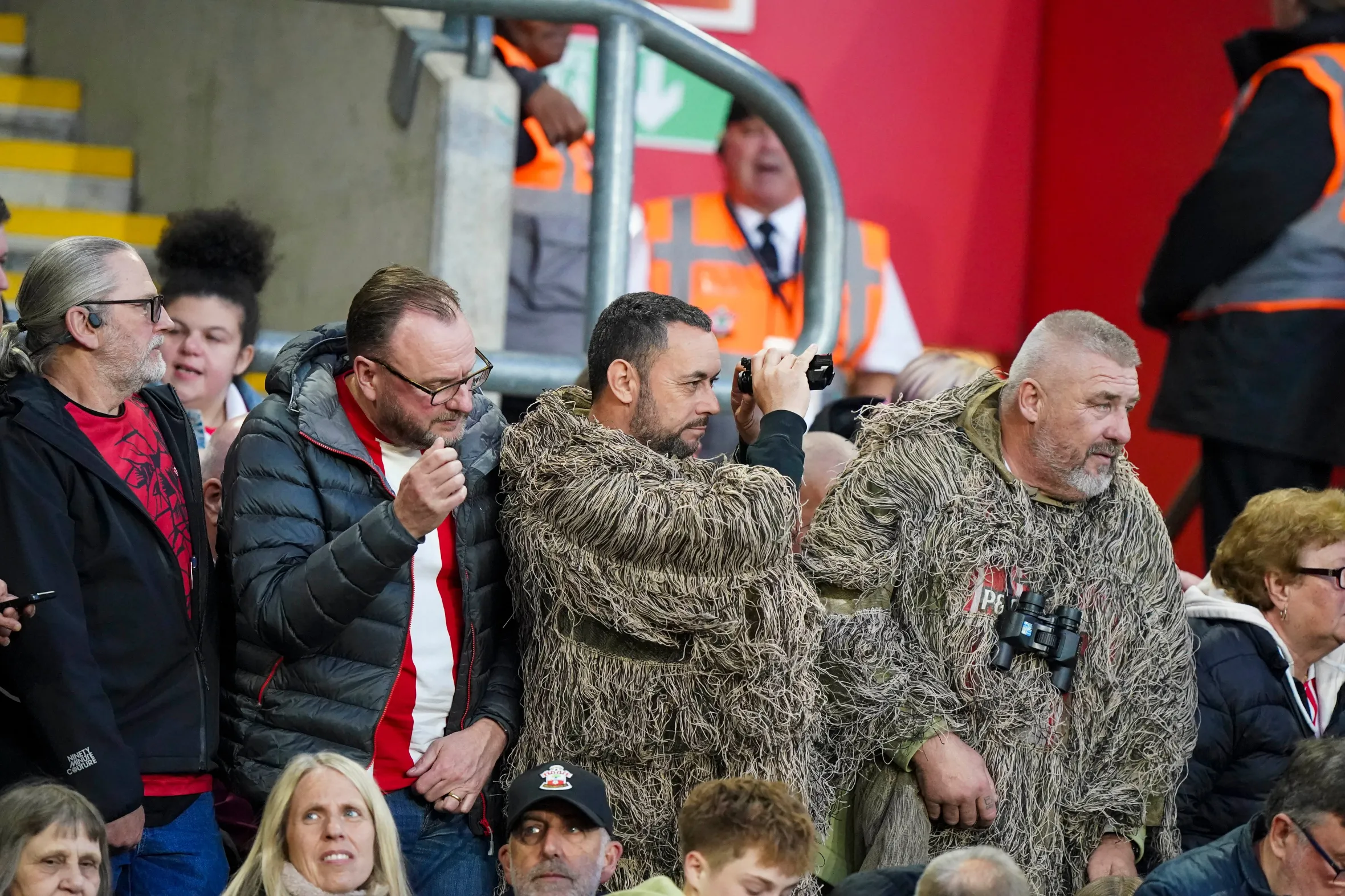 Southampton fans in camouflage and binoculars watching the match.