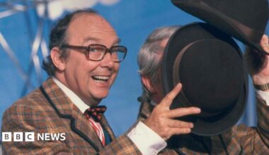Eric Morecambe is grinning as he holds his hat to block Ernie Wise's face during a dance routine