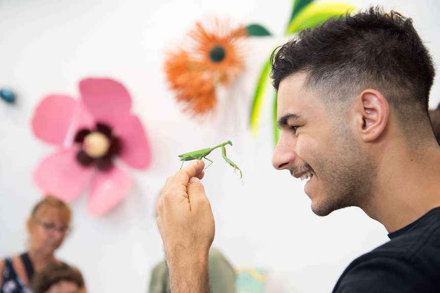 A man smiling and holding a praying mantis.