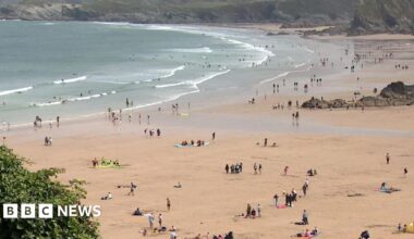 Dozens of people on a sandy beach as the waves crash along the coast.