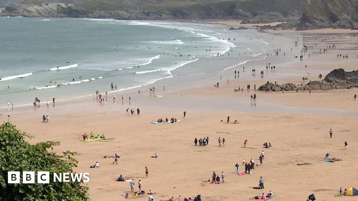 Dozens of people on a sandy beach as the waves crash along the coast.