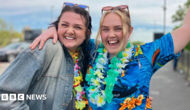 Rob and Nikki Brookes. They are dressed in bright blue shirts with Hawaiian-style flowers around their necks. They have their fists in the air in celebration.