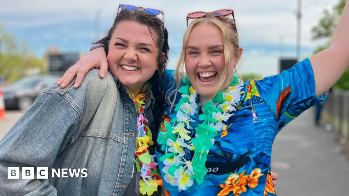 Rob and Nikki Brookes. They are dressed in bright blue shirts with Hawaiian-style flowers around their necks. They have their fists in the air in celebration.