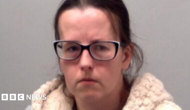A police custody image of Emma Barnett. She has dark brown hair pulled back from her head and black framed glasses. She is wearing a crime gilet over a grey T-shirt.